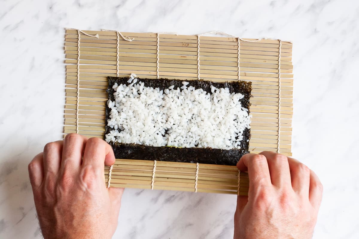 A hand is rolling the sushi using the bamboo mat.