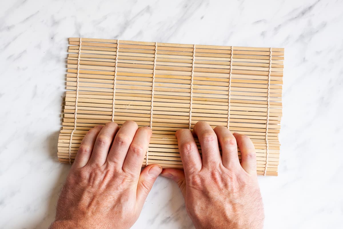 A hand is covering the rolled sushi with the bamboo mat.