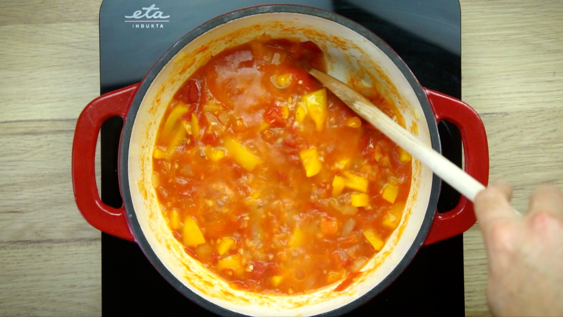 White stockpot with yellow bell peppers and red tomato slices in a thin stew.
