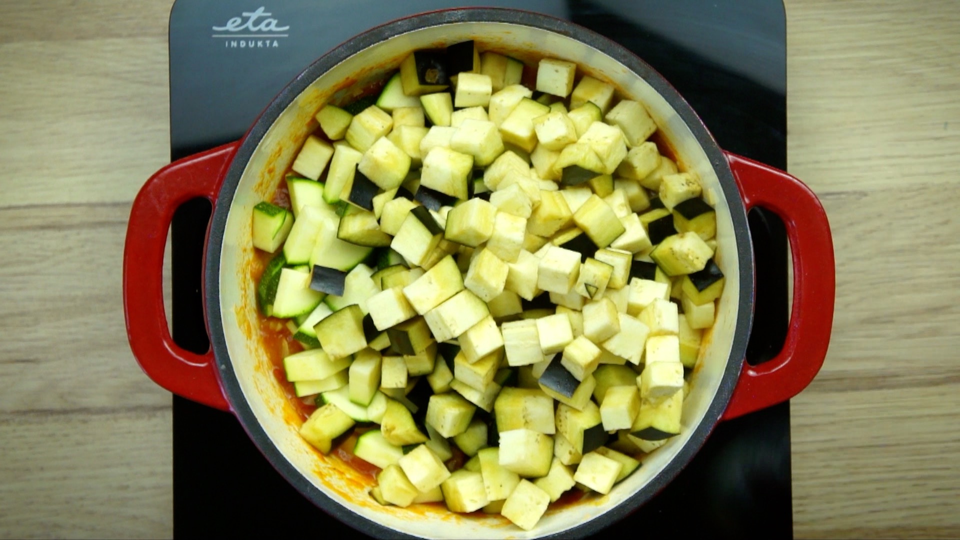 White stockpot with eggplant and zucchini cubes on top of a red stew.