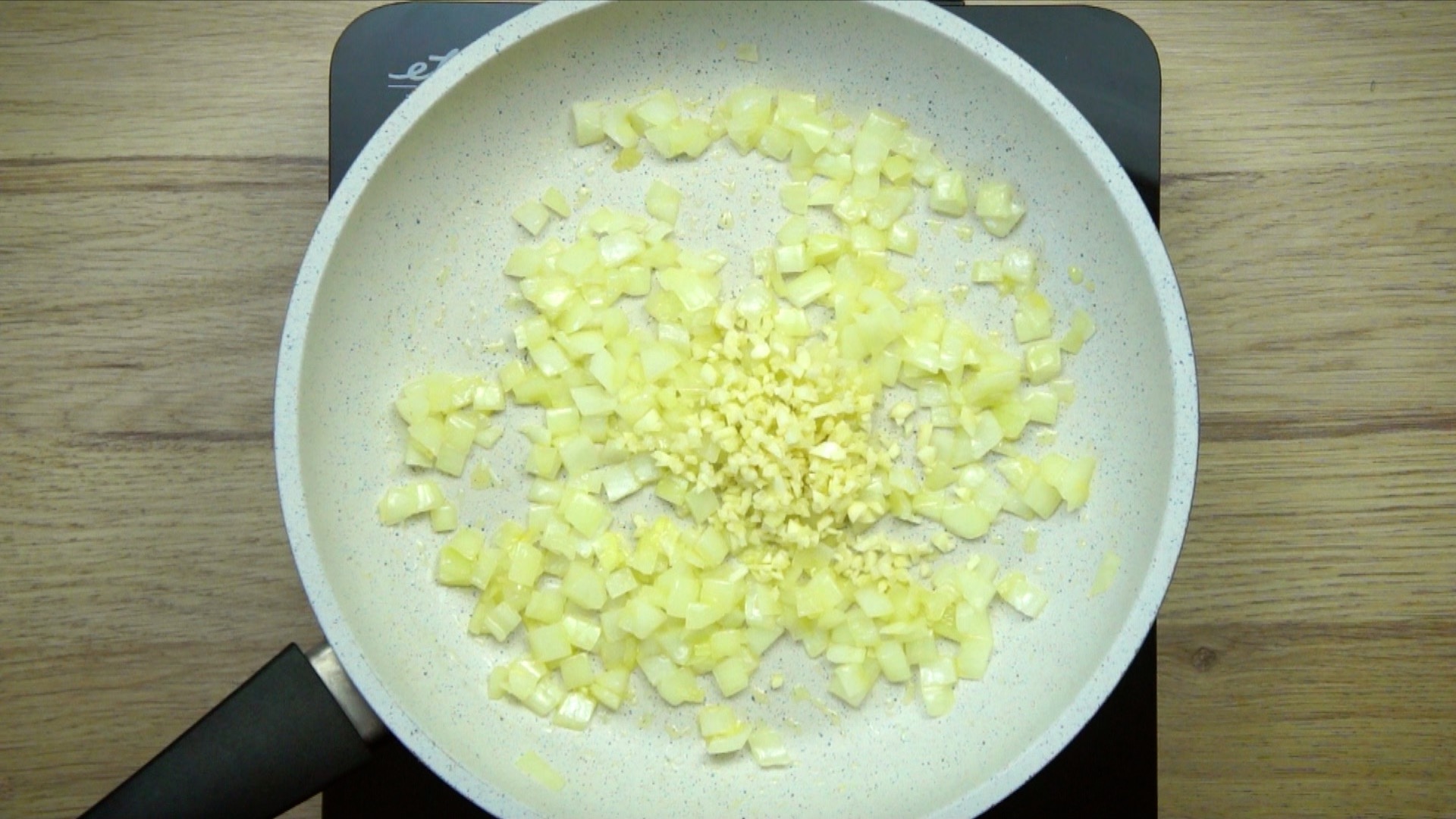 White frying pan with sauteed onion and a small heap of minced garlic. 