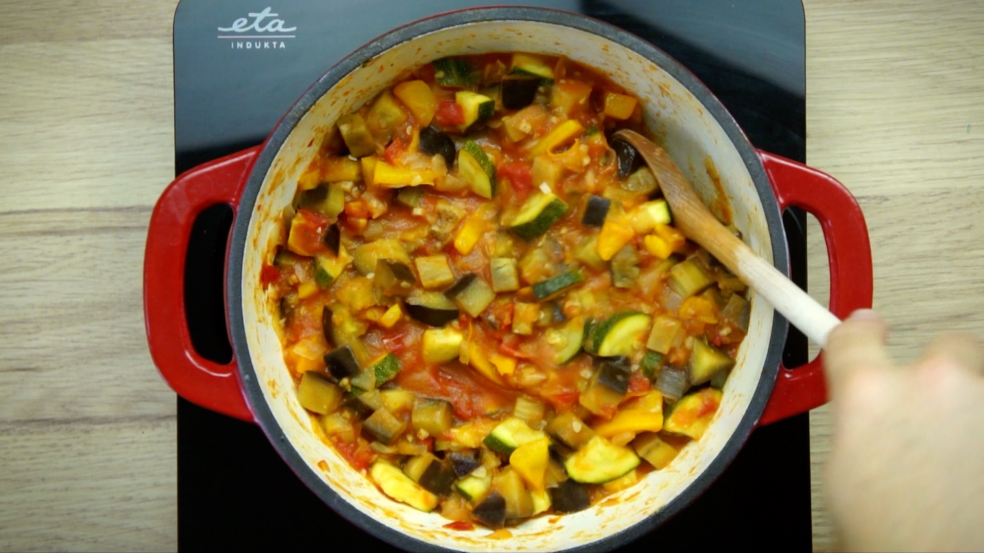 White stockpot with red vegetable stew with eggplant, zucchini, yellow bell pepper and tomato.