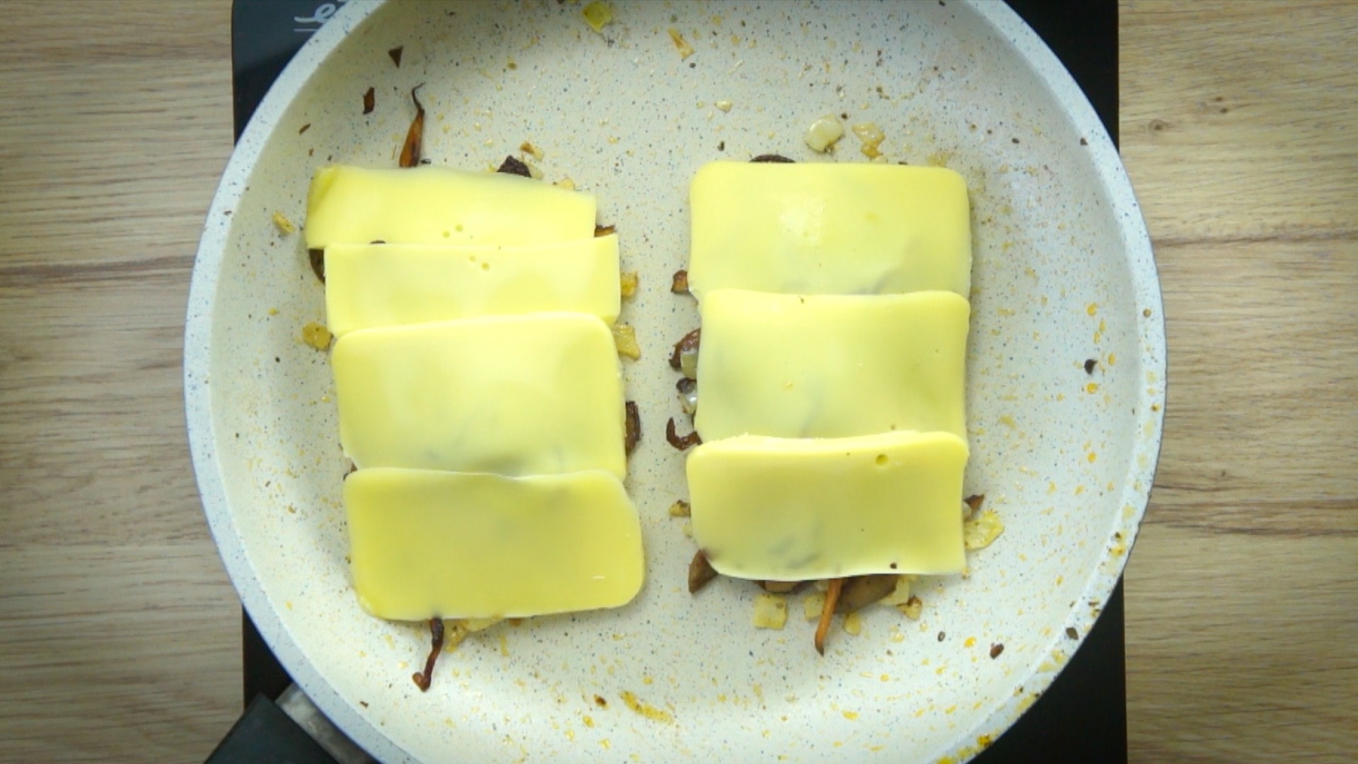 Shredded mushrooms separated into two parts covered with cheese slices in a white frying pan.