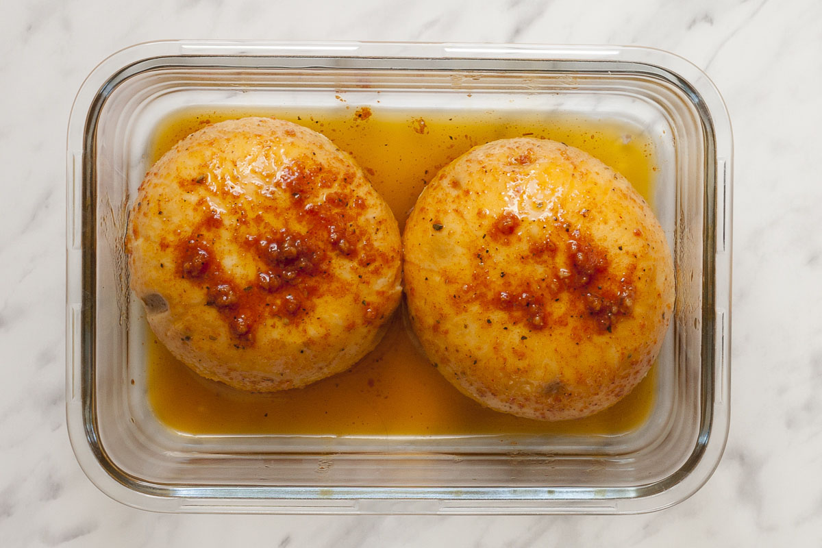 Two large mushroom caps marinating in an oil spice mix in a glass container.
