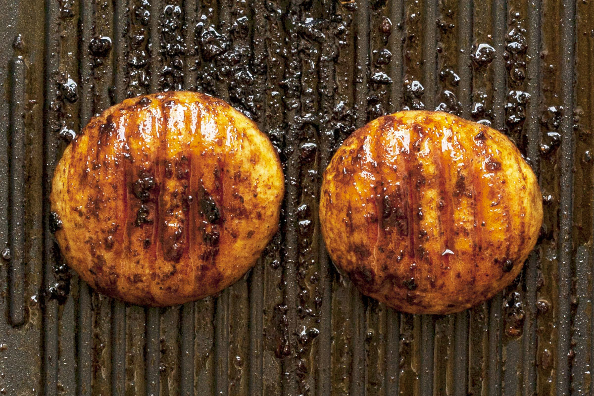 Two large mushroom caps in a grill pan with crispy charcoal lines.