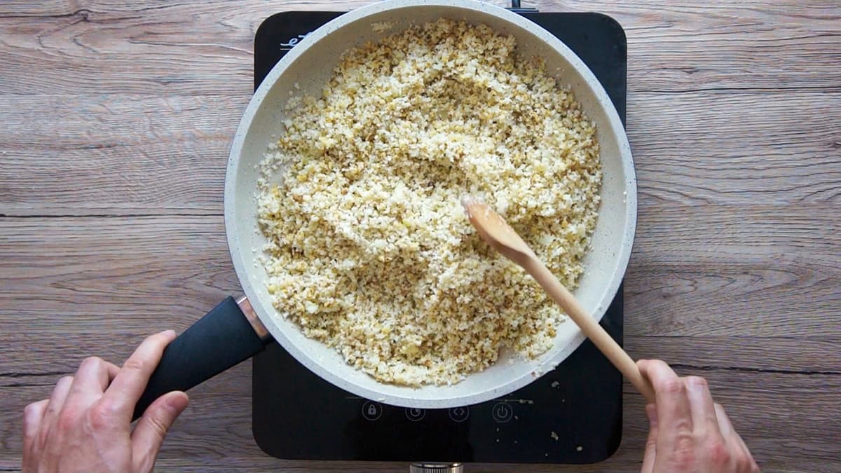White frying pan with chopped cauliflower and walnuts.