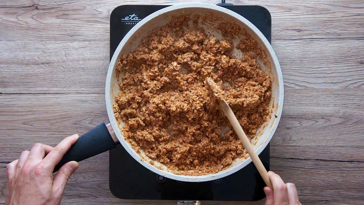 White frying pan with chopped cauliflower and walnuts in a red sauce.