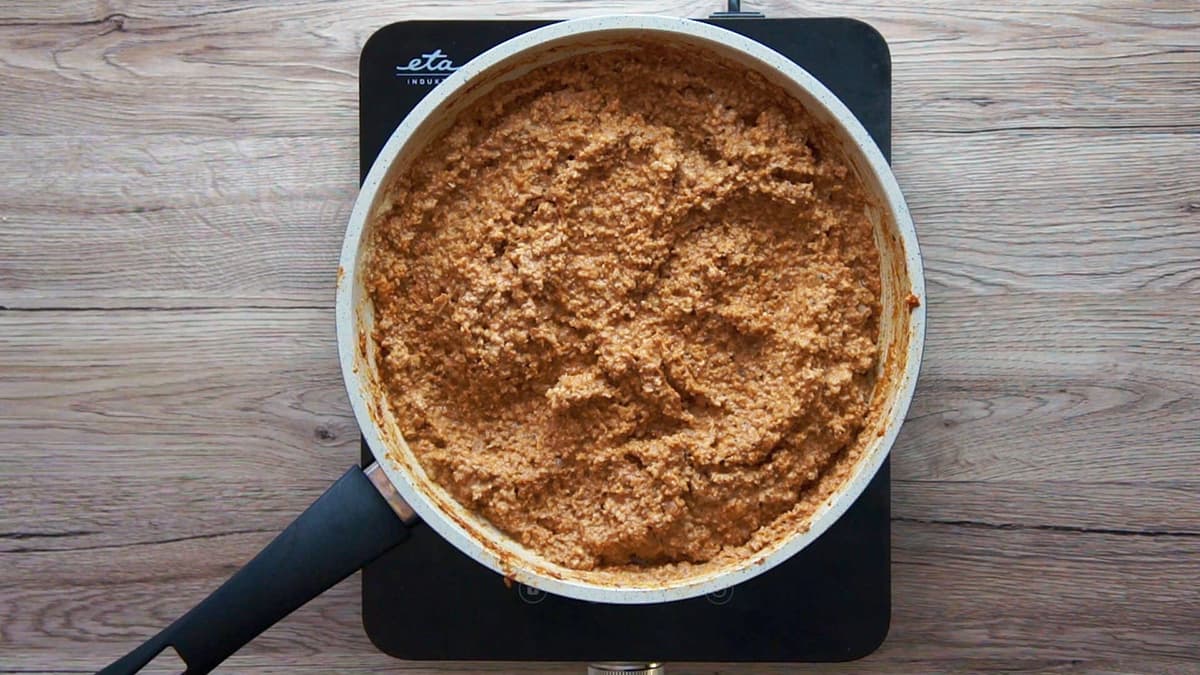 White frying pan with chopped cauliflower and walnuts in a thick red sauce.