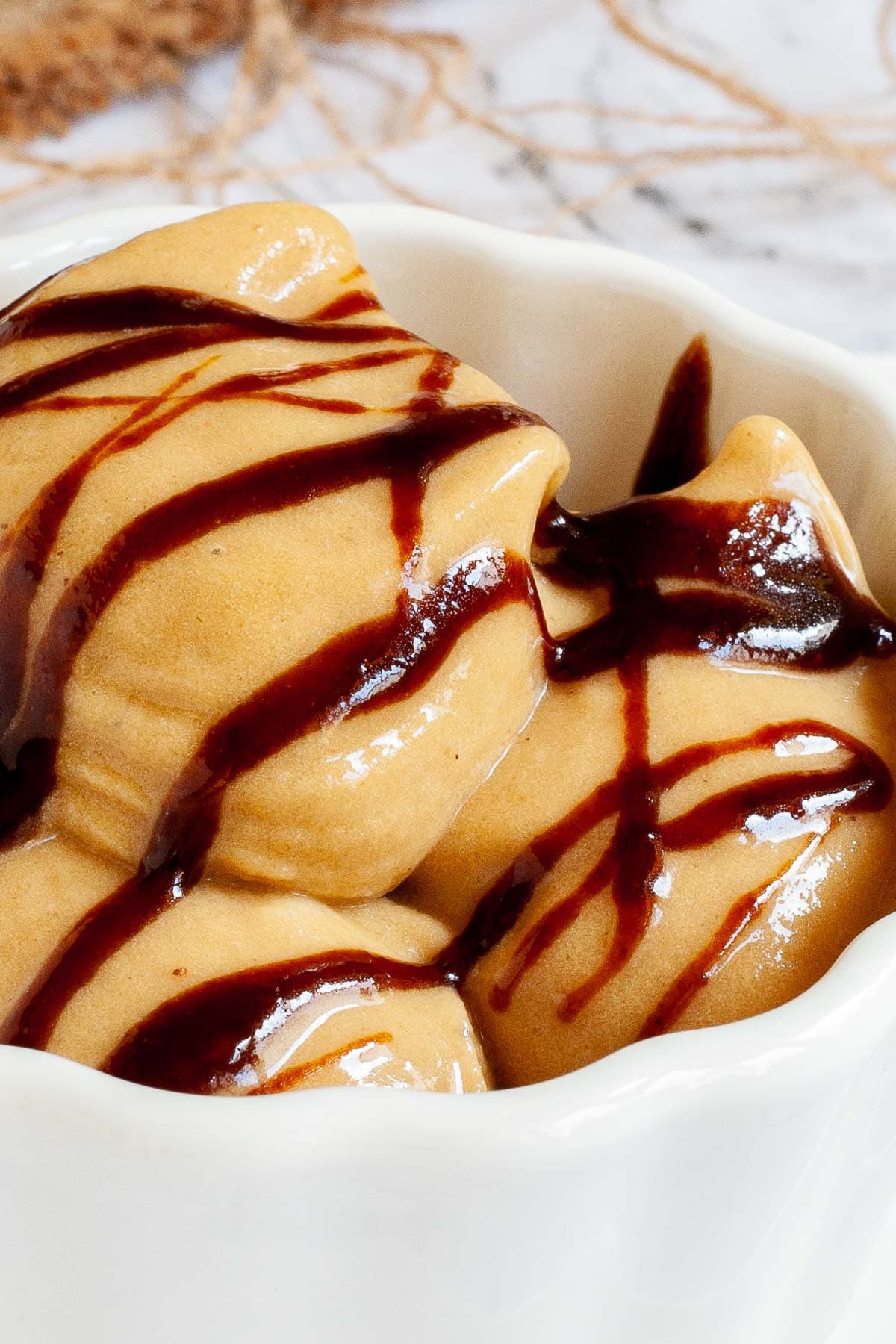 A white bowl of caramel colored ice cream with dark brown caramel drizzle on top.
