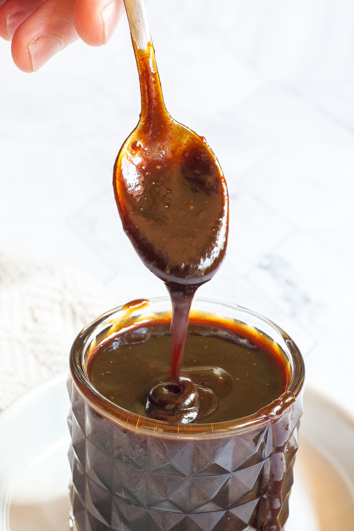 Dark brown caramel sauce in a glass bowl. Caramel is flowing off a spoon.
