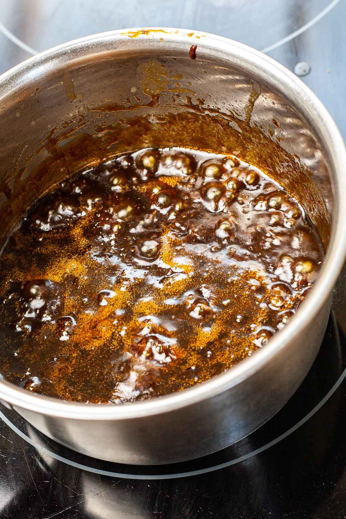 Dark brown sauce is bubbling in a small silver saucepan.