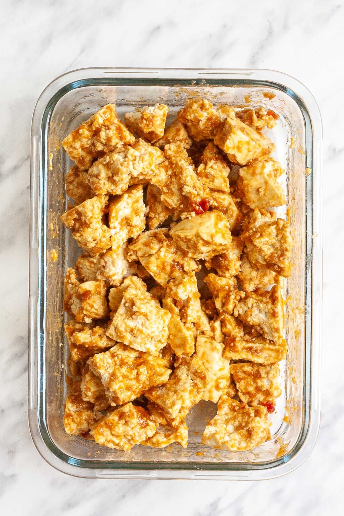 Glass bowl with tofu bites marinating in a yellow brown sauce