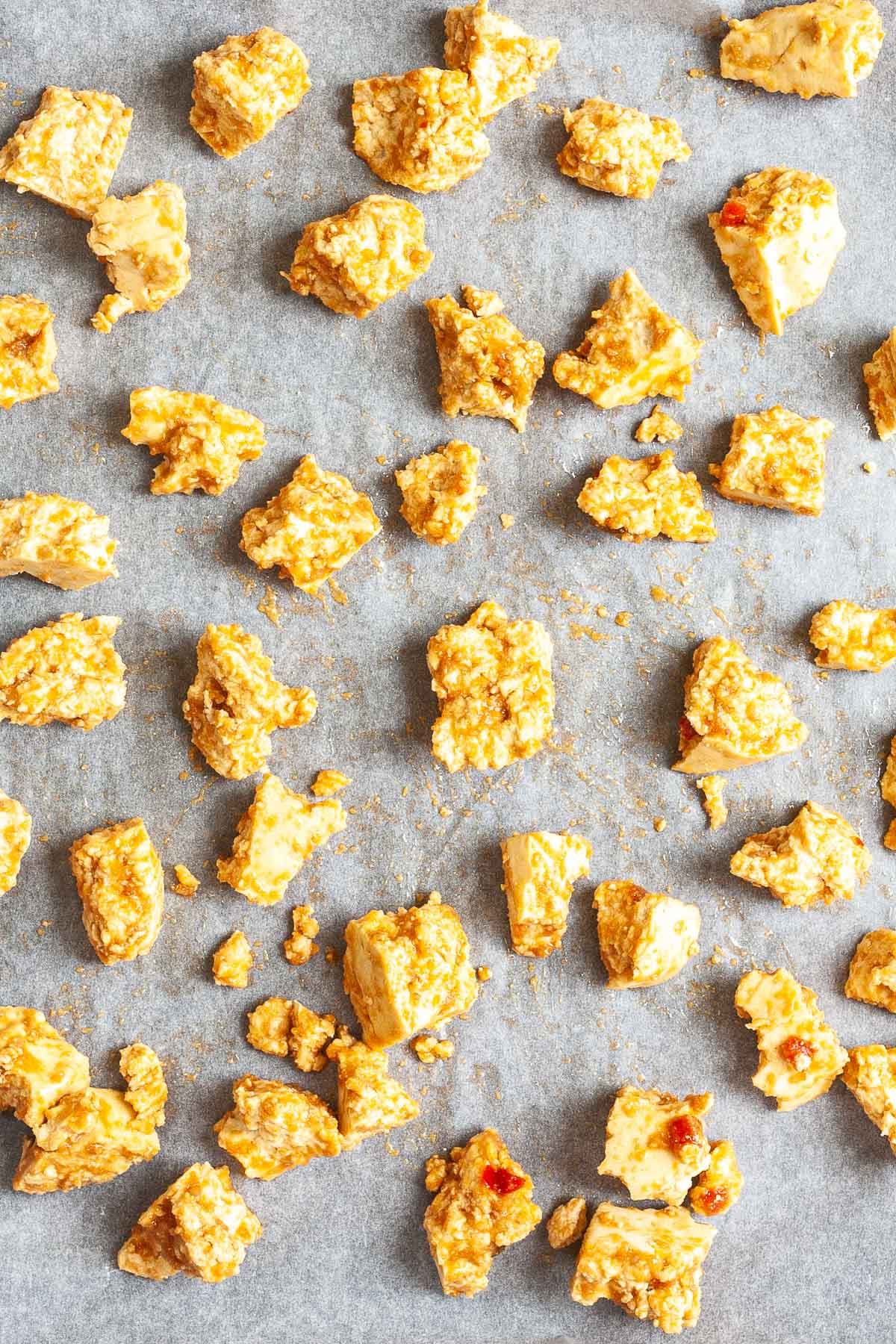 Torn tofu bites in a yellow brown sauce is placed in a parchment paper.