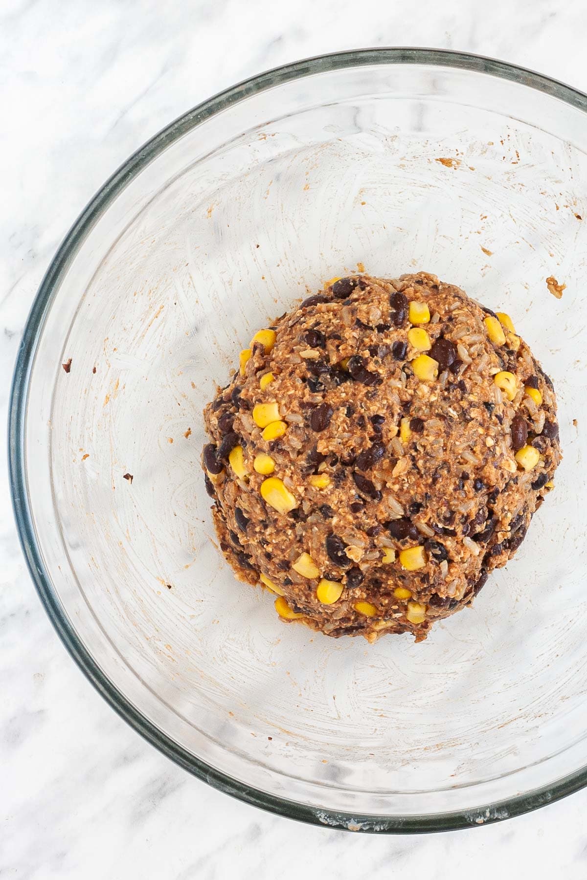 Brown burger patty mixture is forming a ball in the middle of the glass bowl.