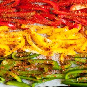 Red yellow green bell pepper and mushroom slices in a sheet pan seasoned with different spices before baking