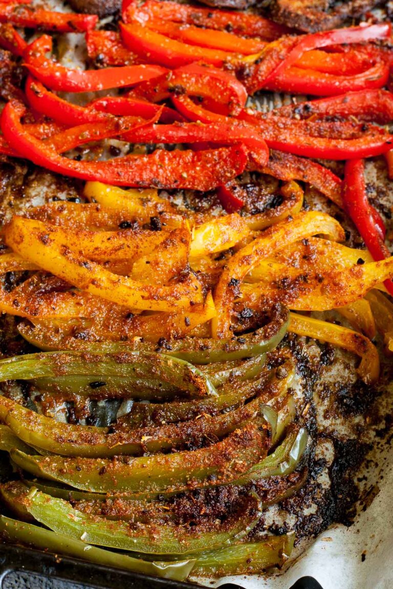 Close-up of roasted brown crispy seasoned red, yellow, green bell pepper strips after baking with tongs taking a couple of them.