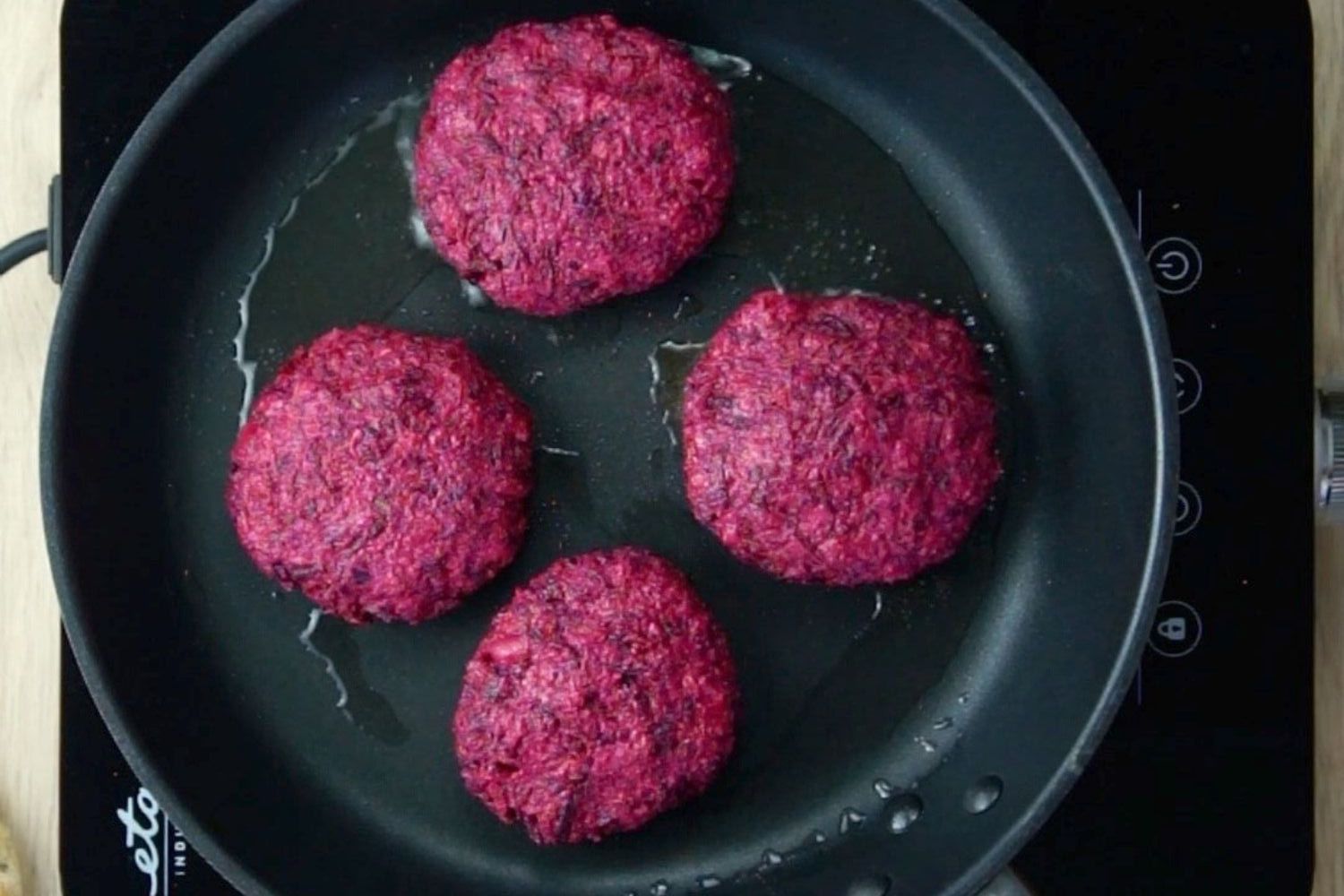 4 purple burger patties in a black fryin pan. 