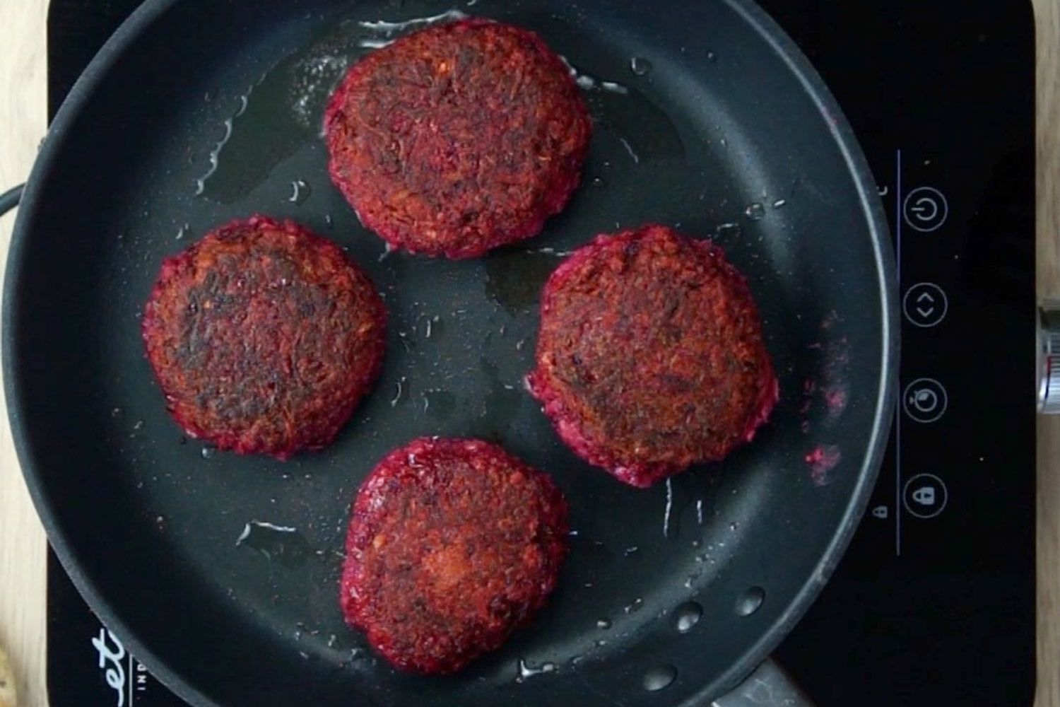 4 crispy purple burger patties in a black frying pan