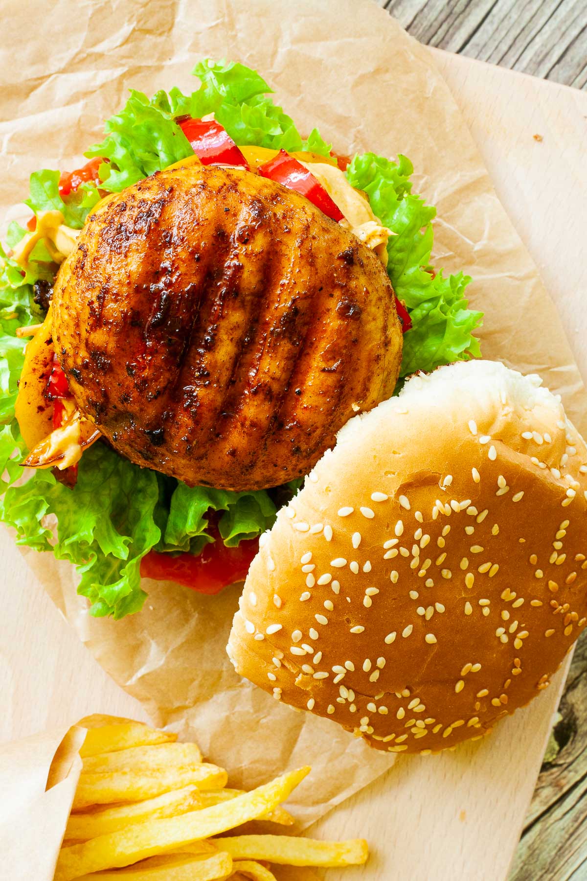 A burger from above with the top bun put on the side. Grilled charcoaled mushroom cap is on the top with lettuce, yellow and red sauce and red pepper slices below it.