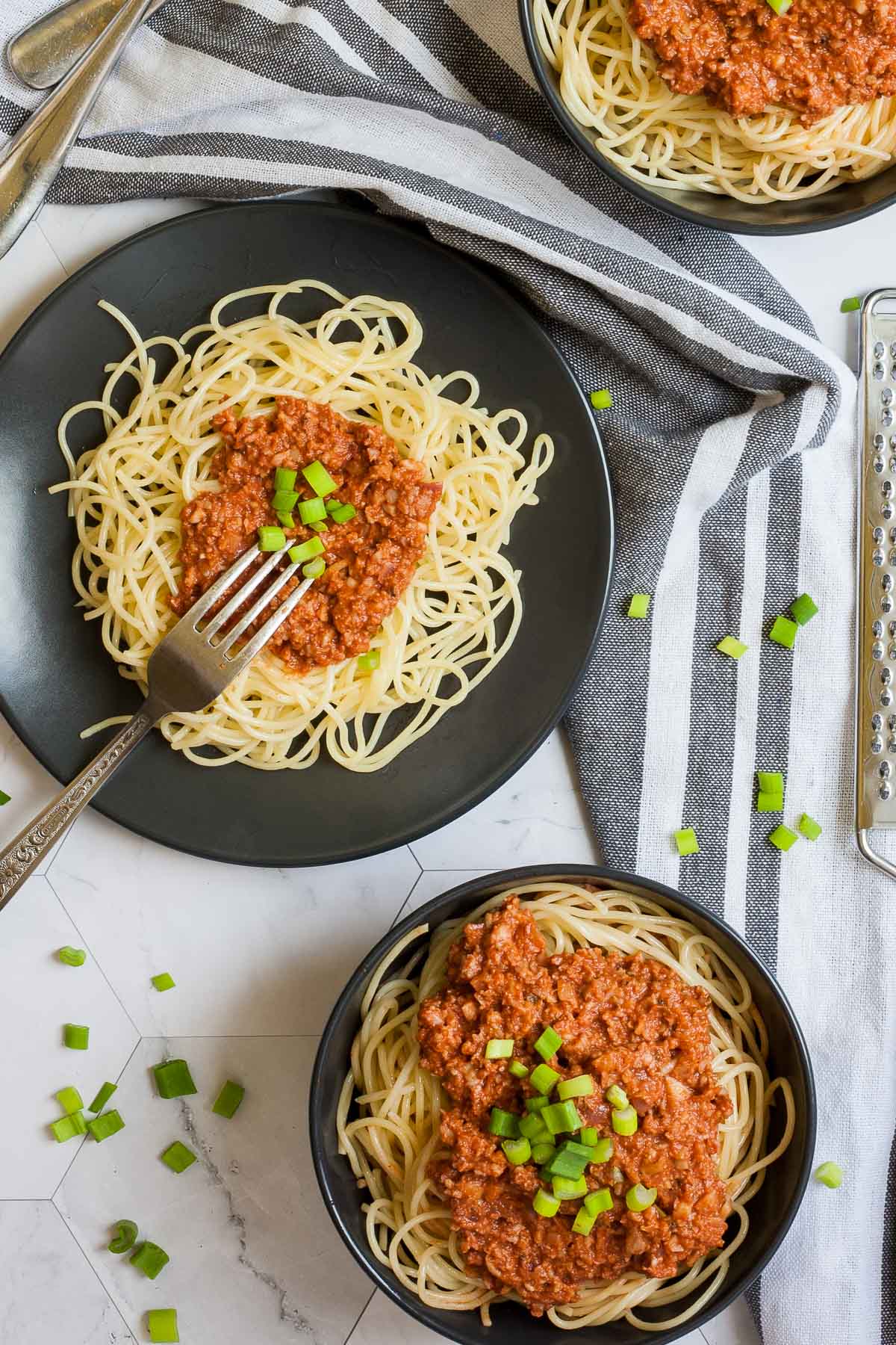 3 black bowls of spaghetti topped with red sauce with fake meat pieces sprinkled with chopped green onion.