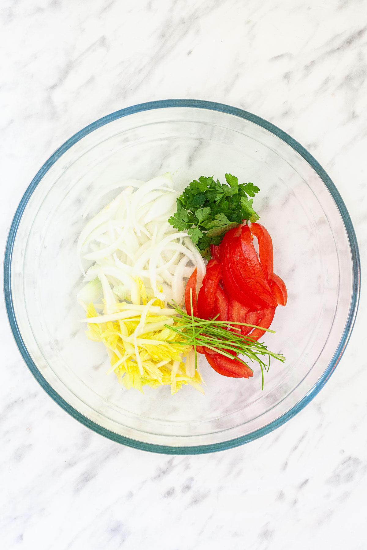 Glass bowl with tomato slices, cilantro, celery, and sliced onion. 
