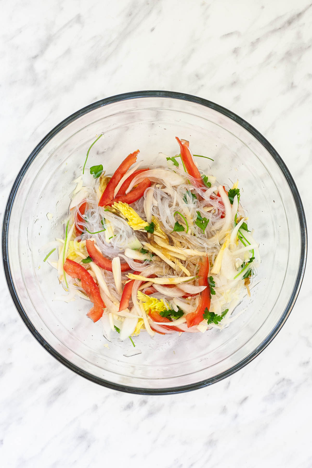 Glass bowl with tomato slices, cilantro, celery, sliced onion and thin glass noodles slightly brown from a thin sauce. 