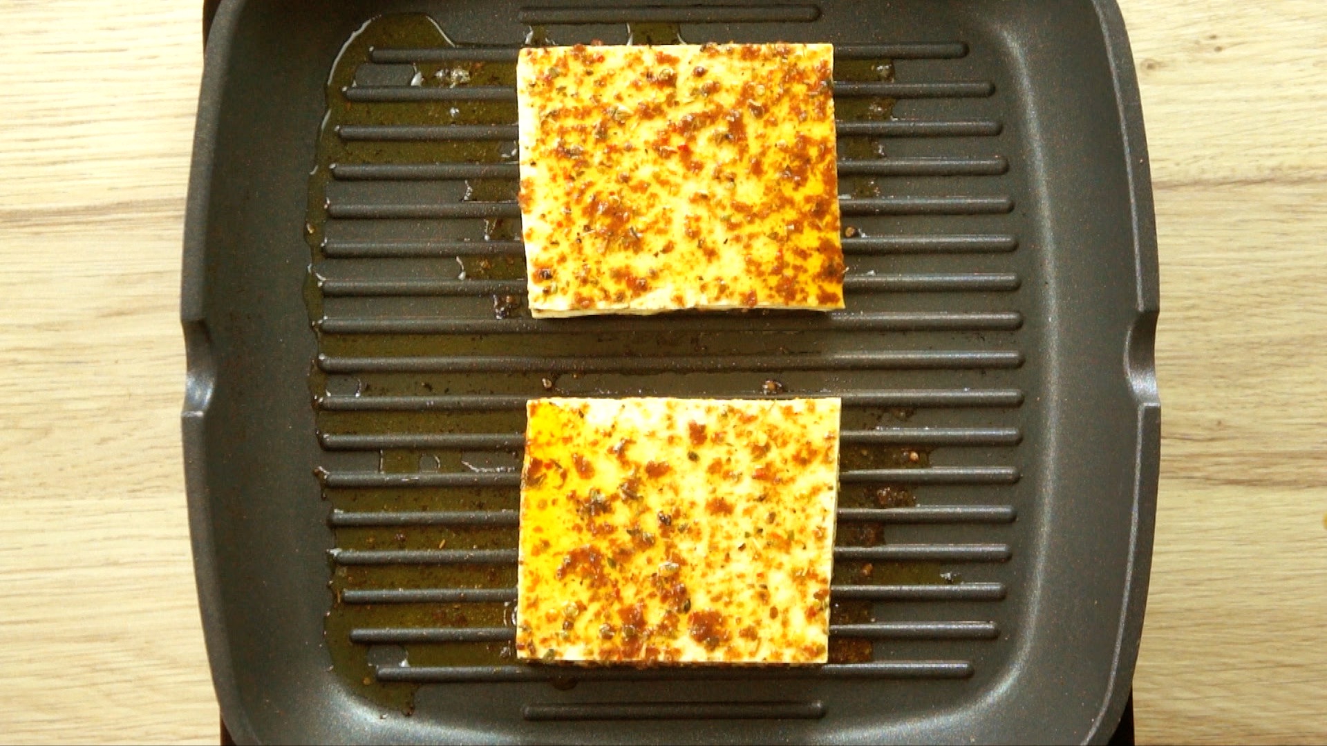 Two large square tofu slices covered in a brownish marinade is placed on a grill pan. 