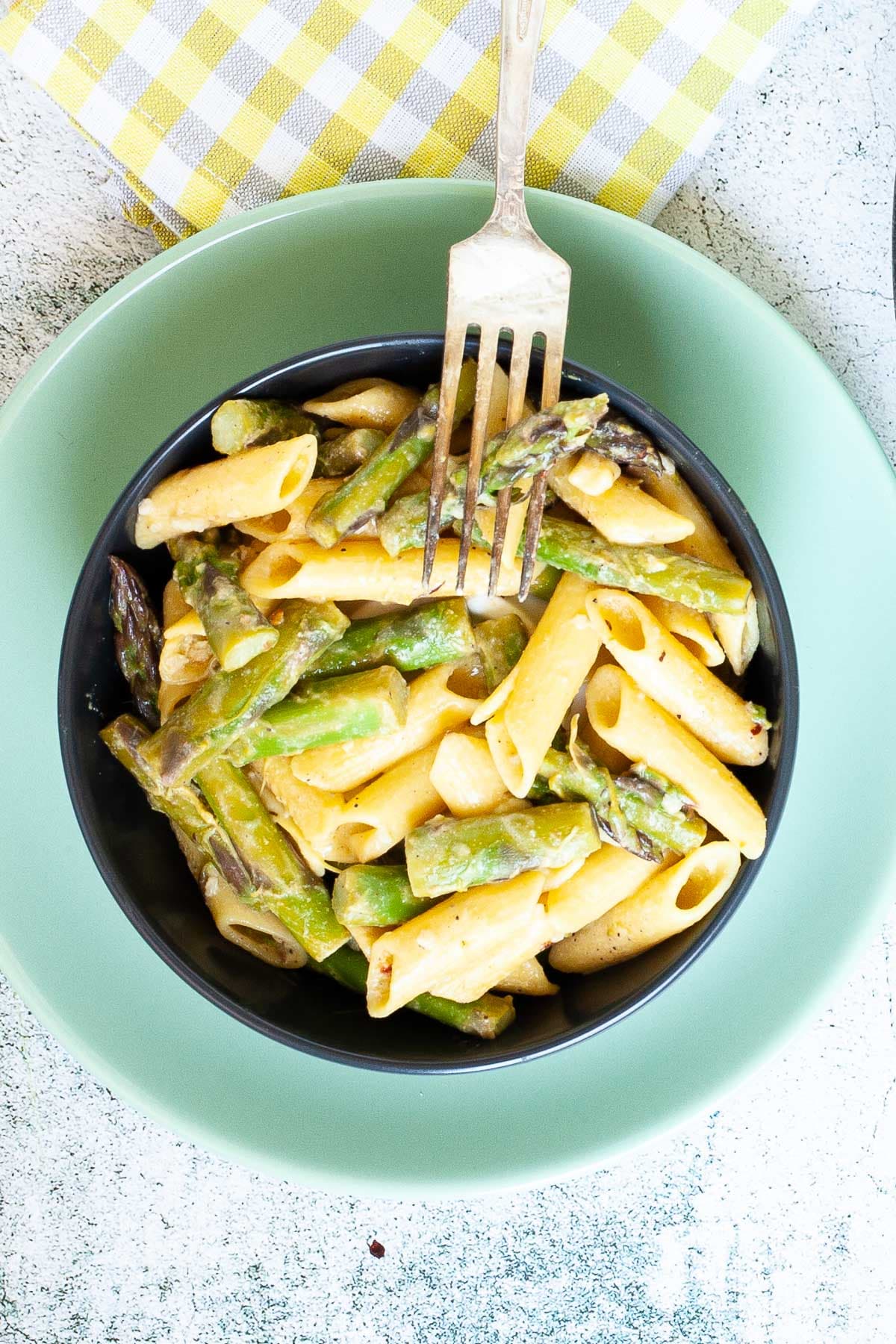 A black bowl with penne pasta and asparagus pieces. 