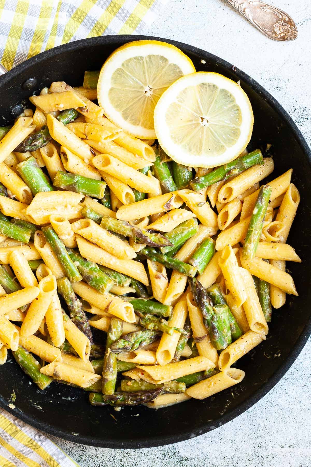 A frying pan with penne pasta, asparagus pieces and 2 lemon slices. 