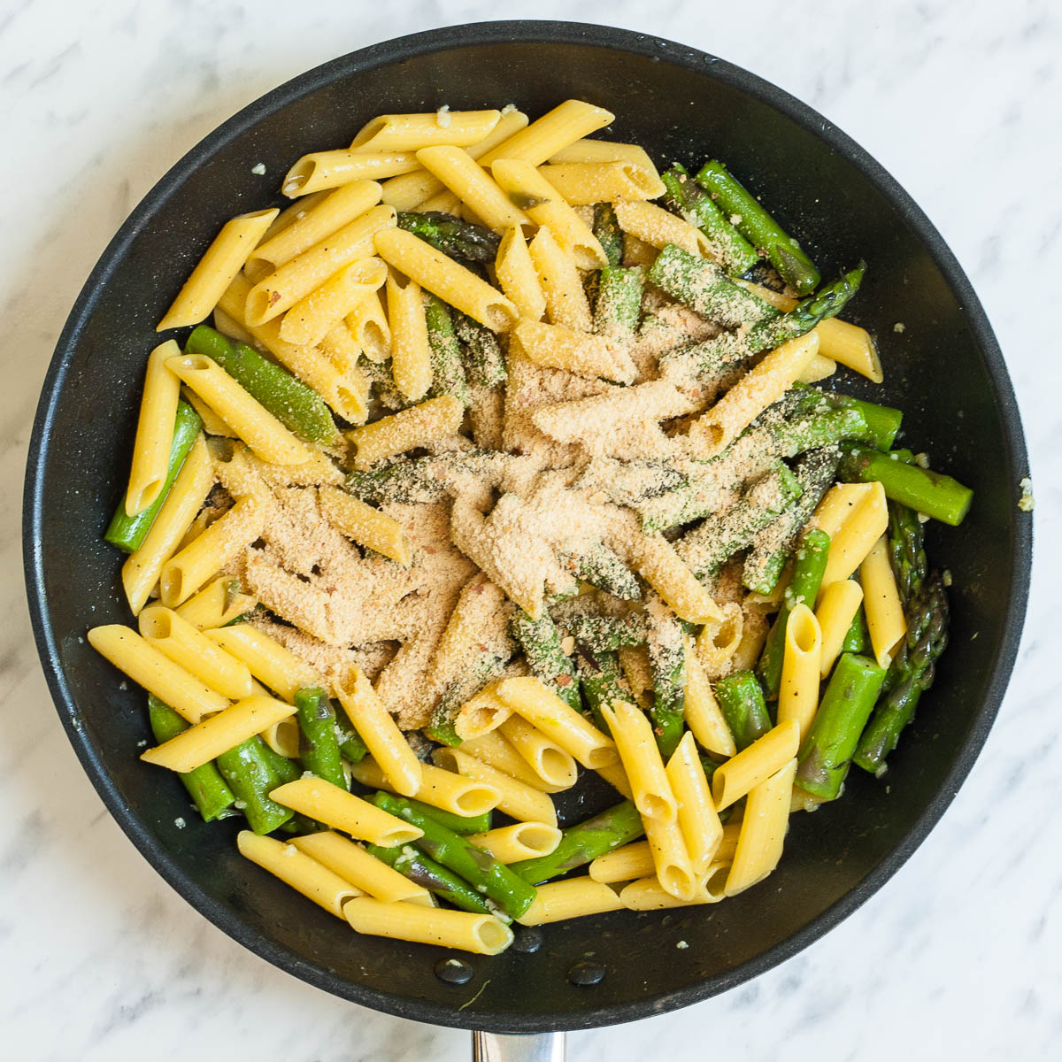 Black frying pan with penne pasta, asparagus and parmesan cheese.