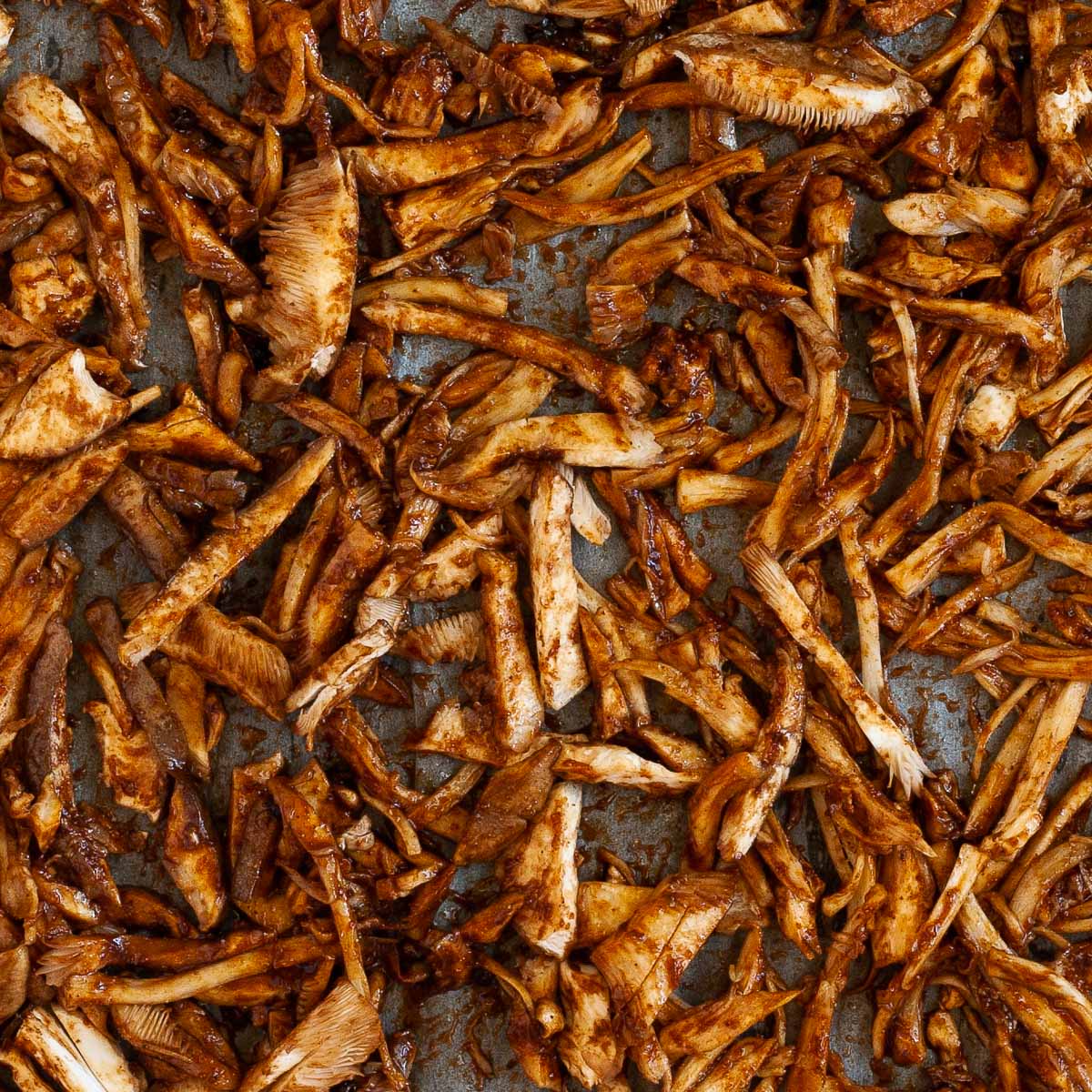 A parchment paper is full of brown saucy shredded mushrooms.