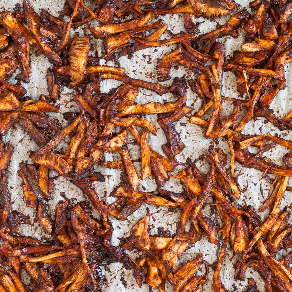 A parchment paper is full of brown saucy crispy shredded mushrooms.