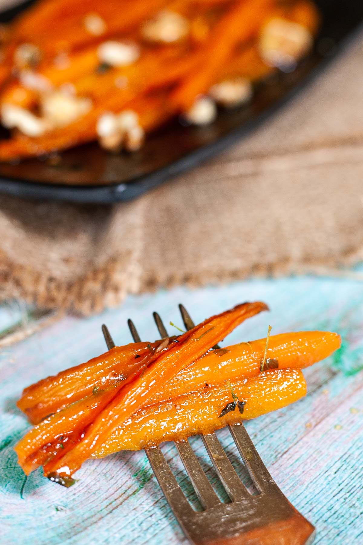 A fork is holding 3 matchstick carrots. A black plate with the rest of the carrots is int he background.