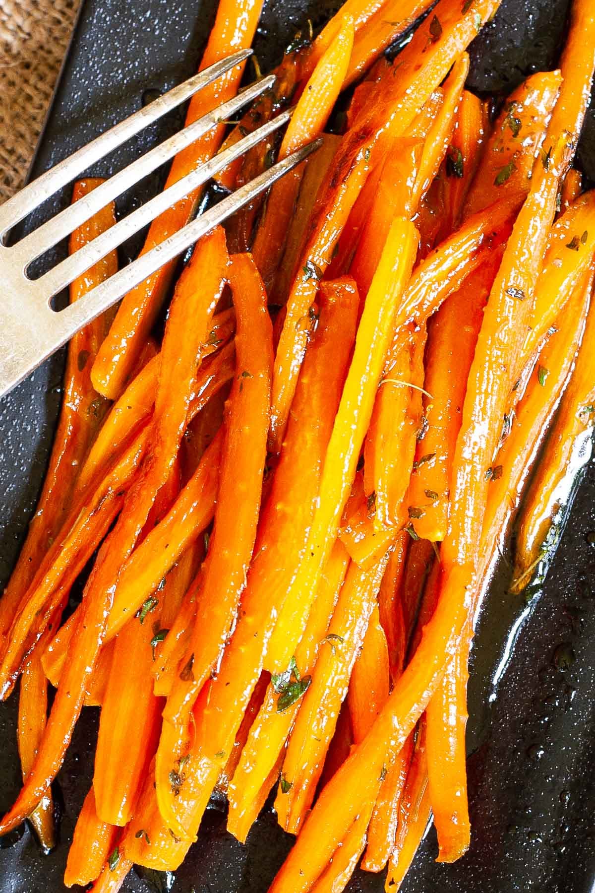 Black rectangular plate with matchstick carrots in glaze. A hand is holding a fork and taking some from the top.