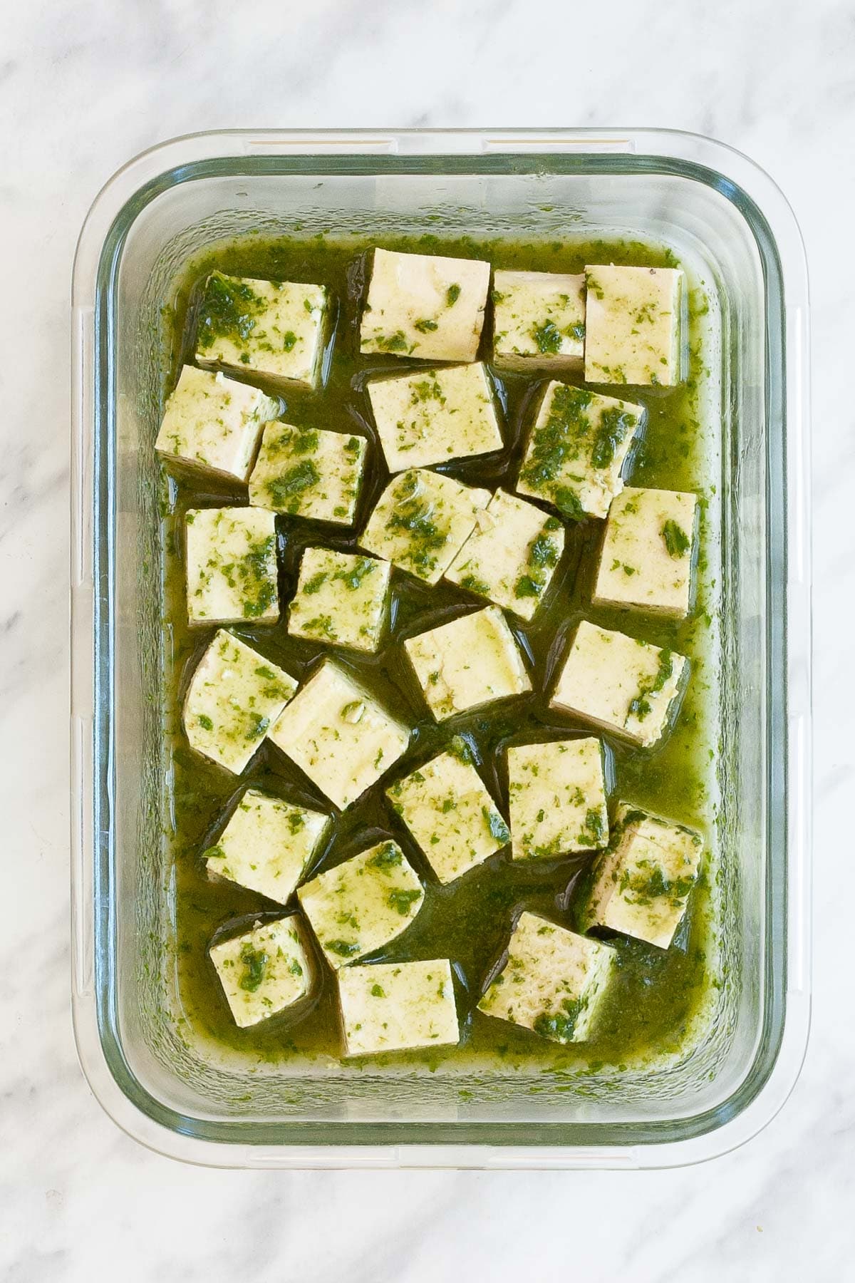 Rectangular glass bowl with white tofu cubes in a green sauce.