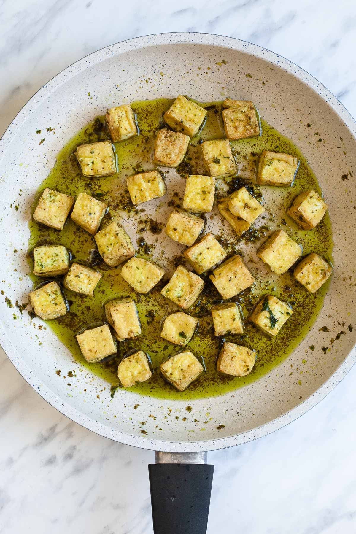 Green-yellow tofu cubes are in a frying pan with a green oily sauce around them.