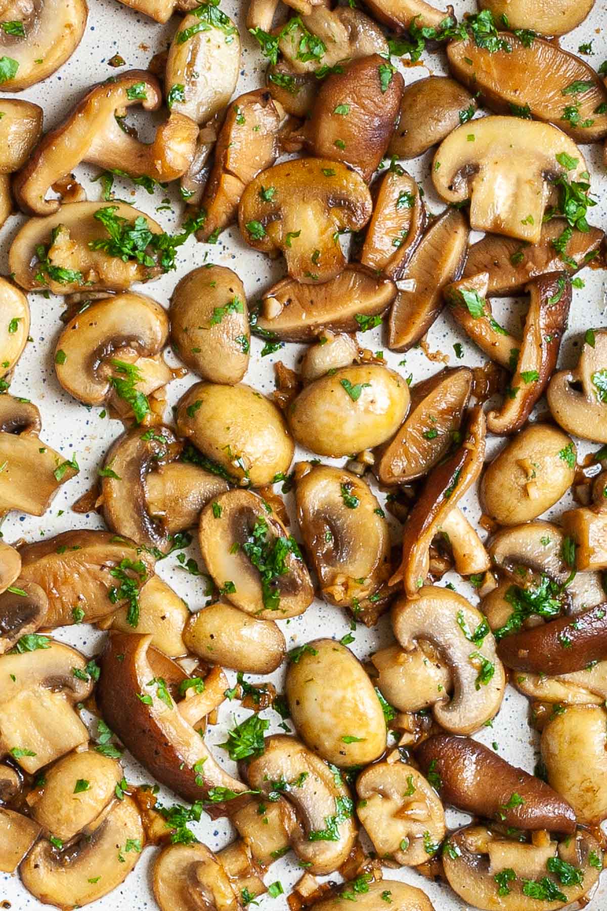 Sliced button and shiitake mushrooms in a frying pan topped with freshly chopped greens.