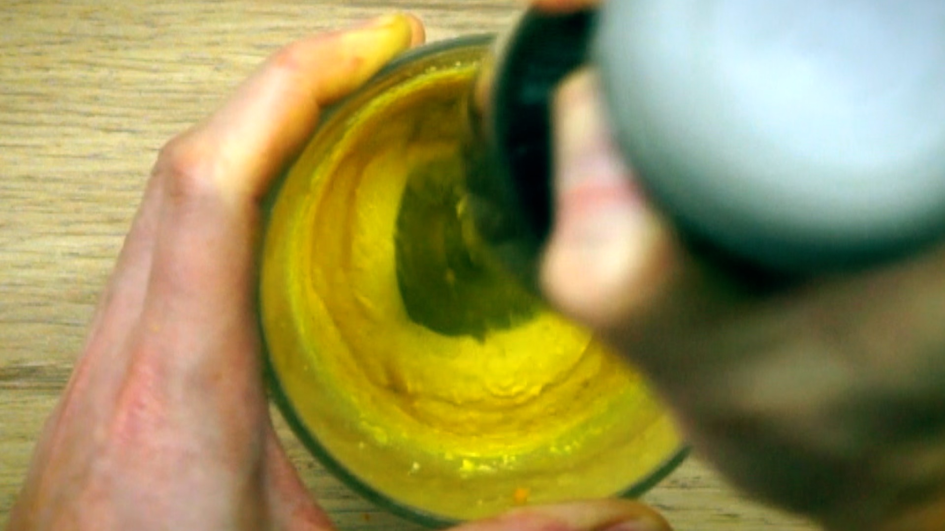 A hand is holding an immersion blender that makes a yellow creamy sauce. 