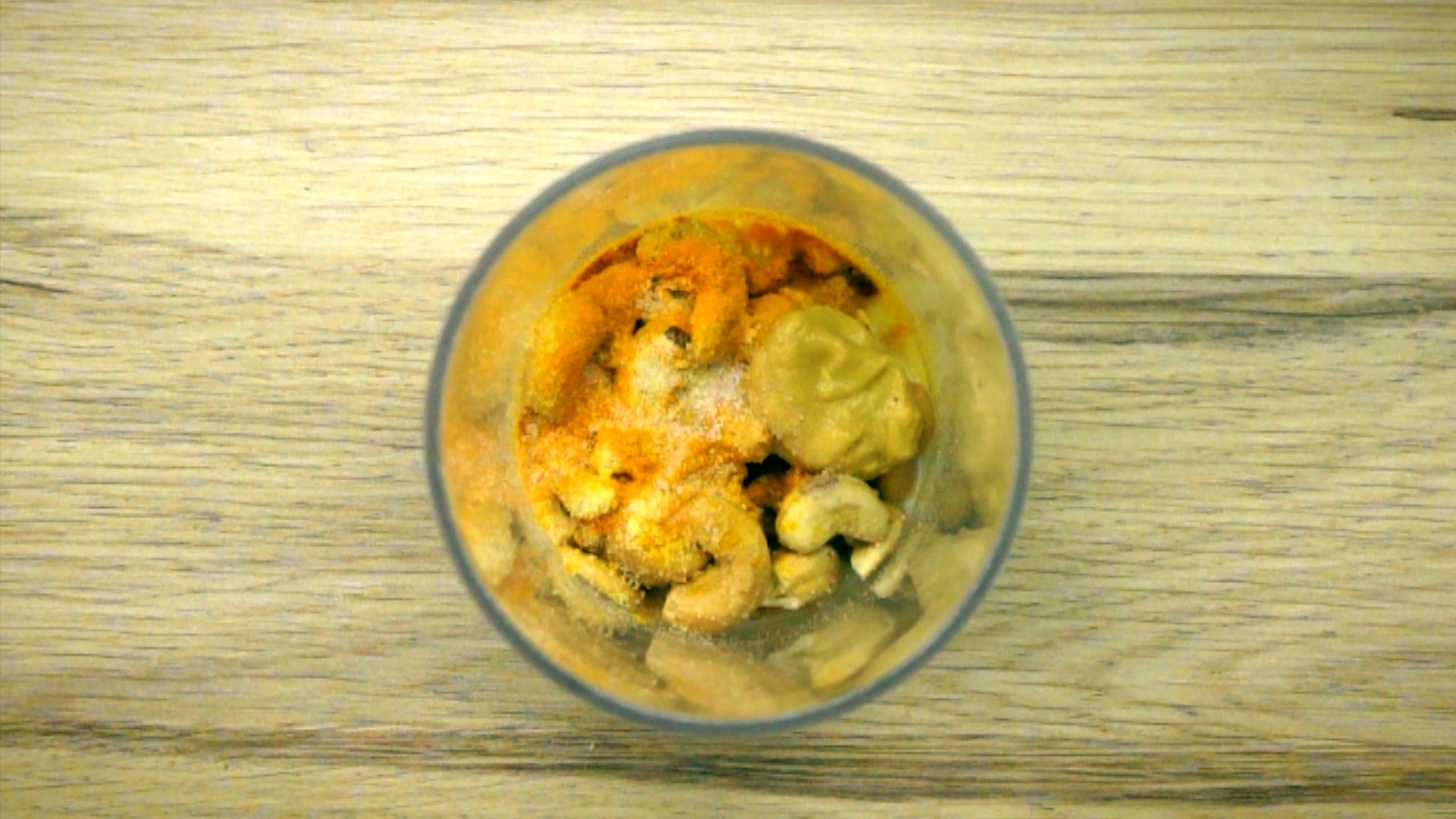 A tall glass container with cashews, mustard, and other spices and flakes. 