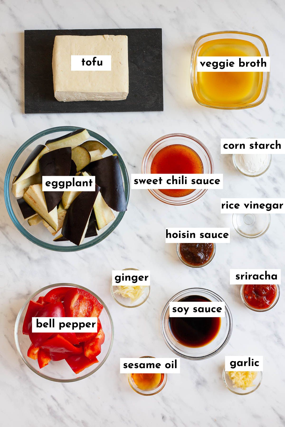 ingredients to make panda express eggplant tofu is in small glass bowls like eggplant chunks, bell pepper slices, veggie broth, red and dark brown liquids, minced ginger and garlic and a block of tofu on a black plate. 