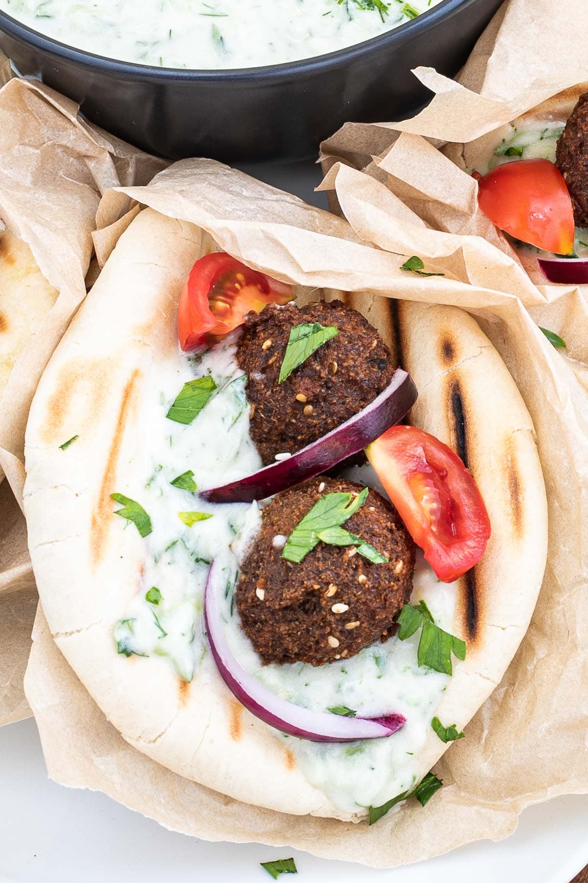 1 pita folded and stuffed with 2 brown falafel balls, white grated cucumber salad, tomato and purple onion slices.