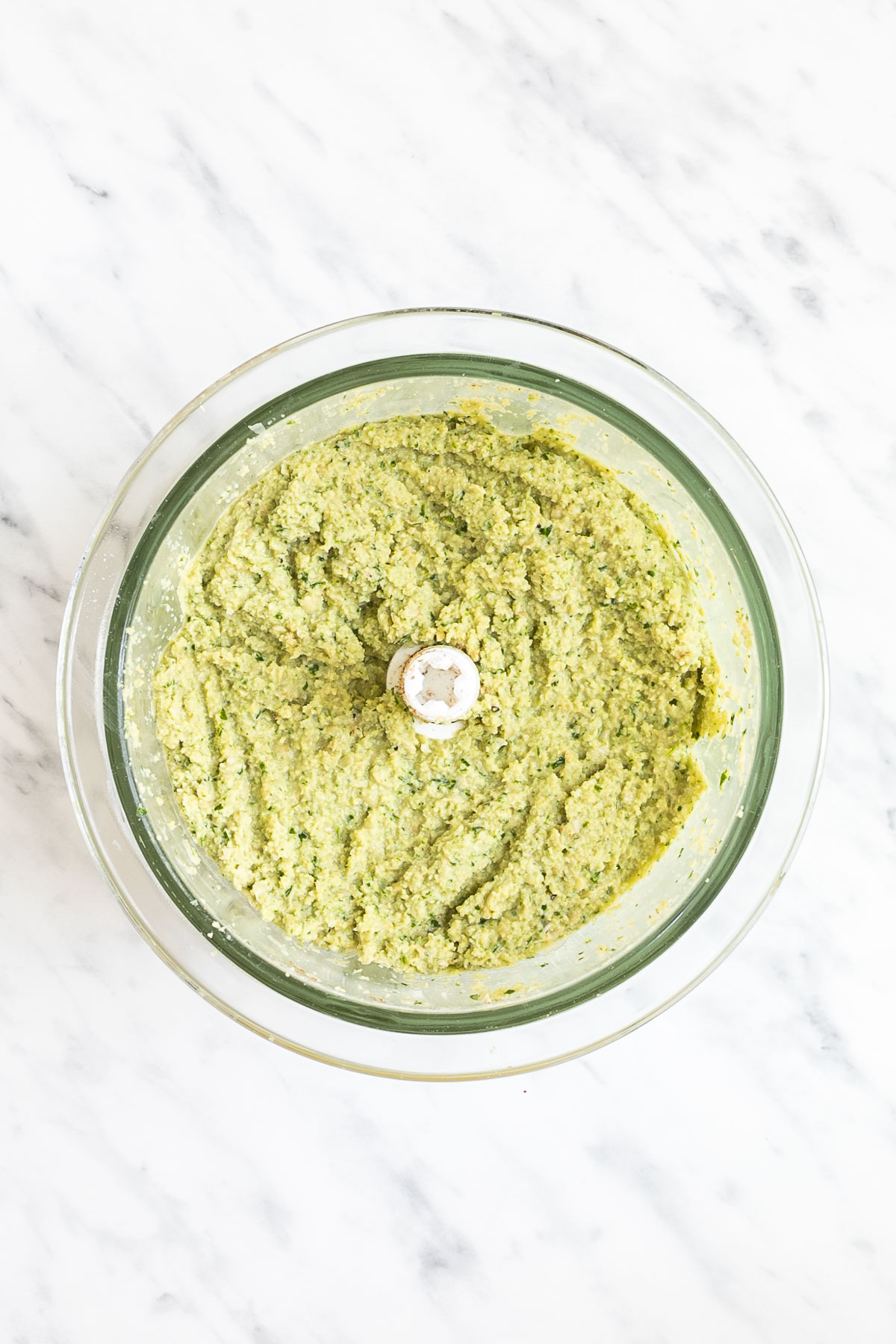 Food processor container from above showing a light green crumbly mixture.