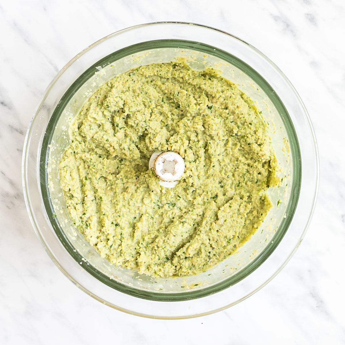 Food processor container from above showing a light green crumbly mixture.