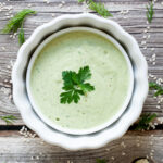 Light green sauce in a white bowl decorated with parsley and dill