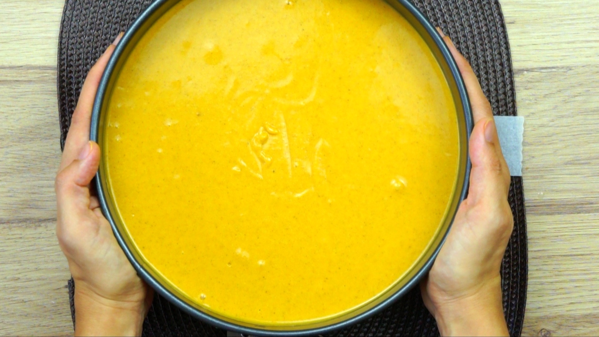 Hands are holding a cake form with smooth orange sauce.