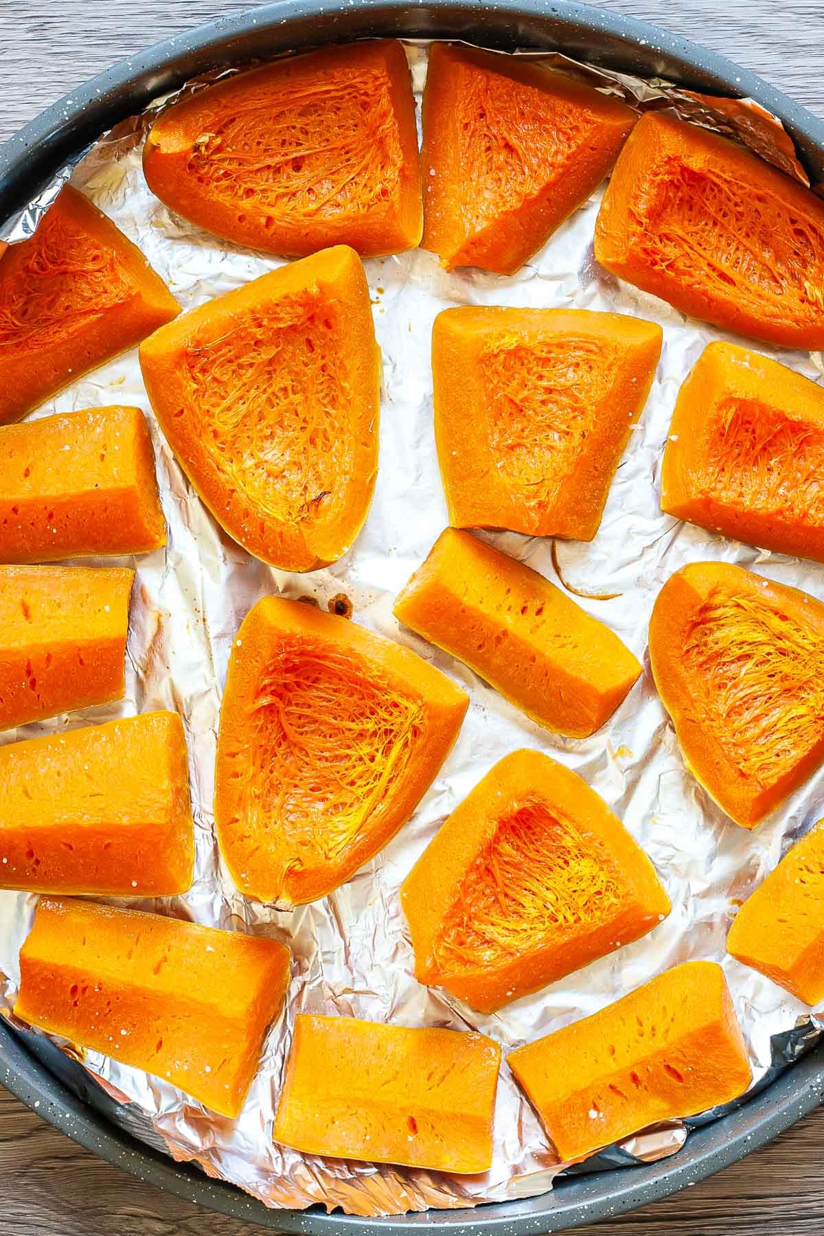 Roasted yellow butternut squash wedges on tin foil in a round pan.