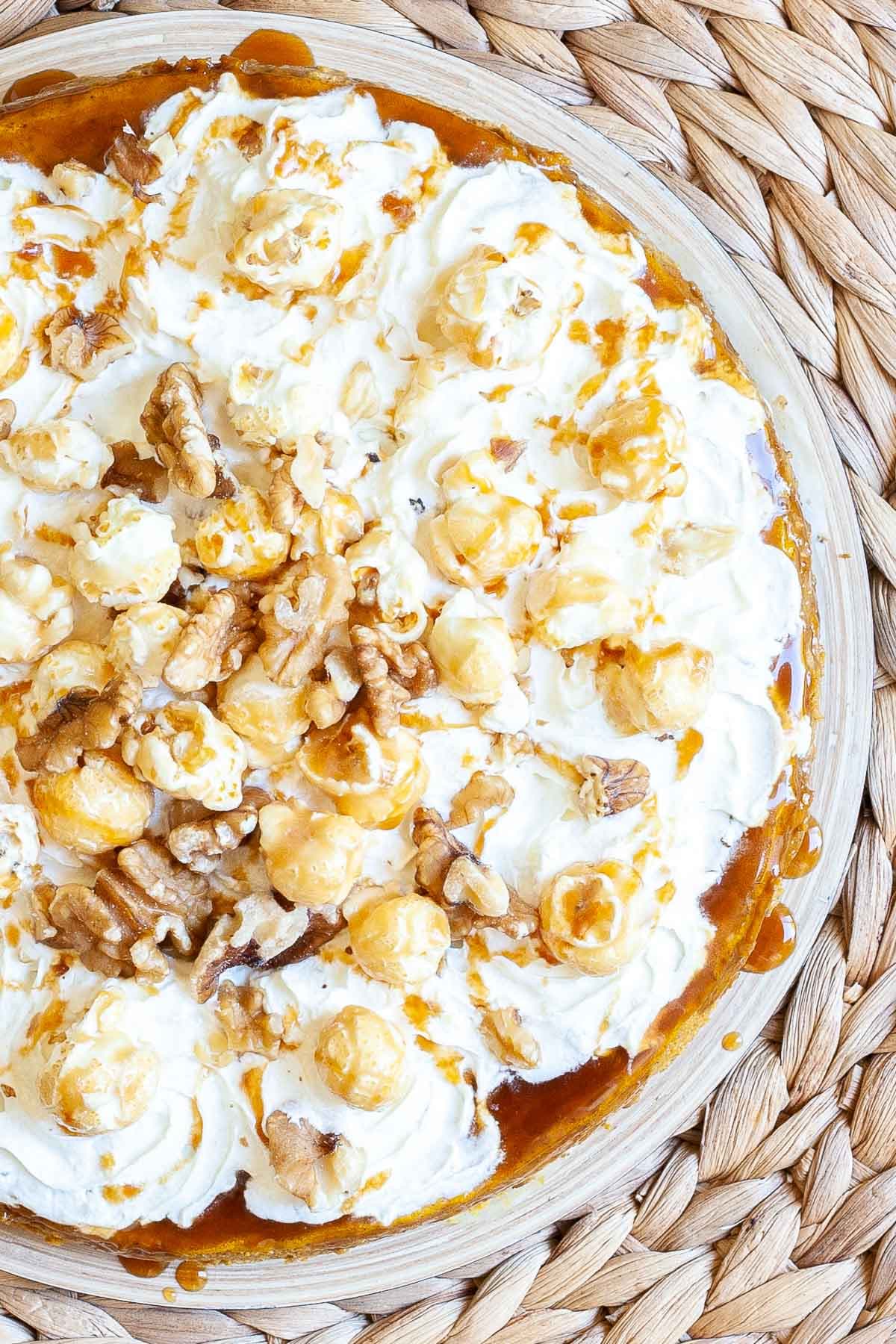 A round cake from above topped with whipped cream, caramel sauce and chopped nuts.