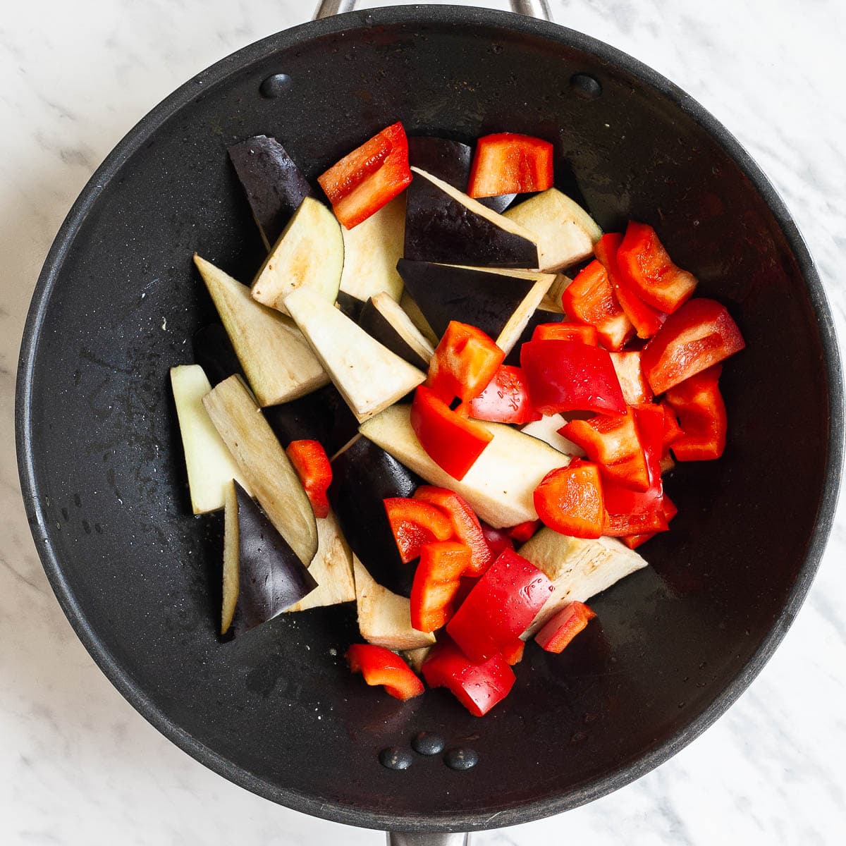 Eggplant slices and red pepper chunks in a wok.