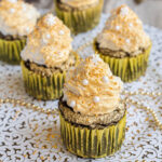 4 dark brownie cupcakes in yellow cupcake liner topped with a white frosting sprayed with gold and sprinkled with gold and white pearl sprinkles and a snowflake one on top.