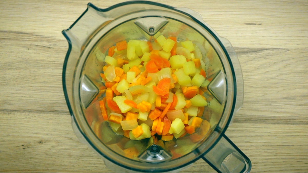 Blender with cooked diced carrots, potatoes, orange sweet potatoes, onions and garlic.